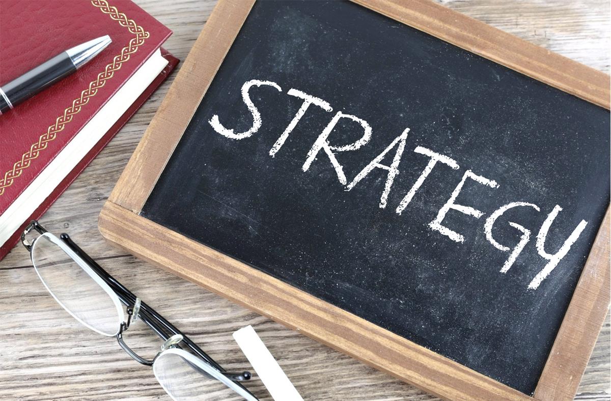 A chalkboard with the word Strategy.  On the left, a book, a pen, and some glasses.